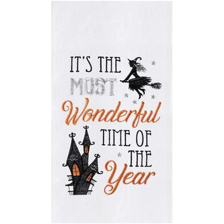 White flour sack towel with the words "it's the most wonderful time of the year" embroidered on it along with a flying witch and a haunted house. 