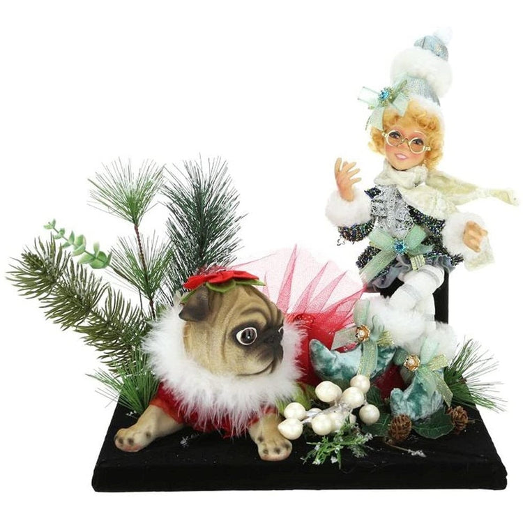 Girl elf wearing blue jacket and hat, sitting next to a pug in red dress, and some pine branches.