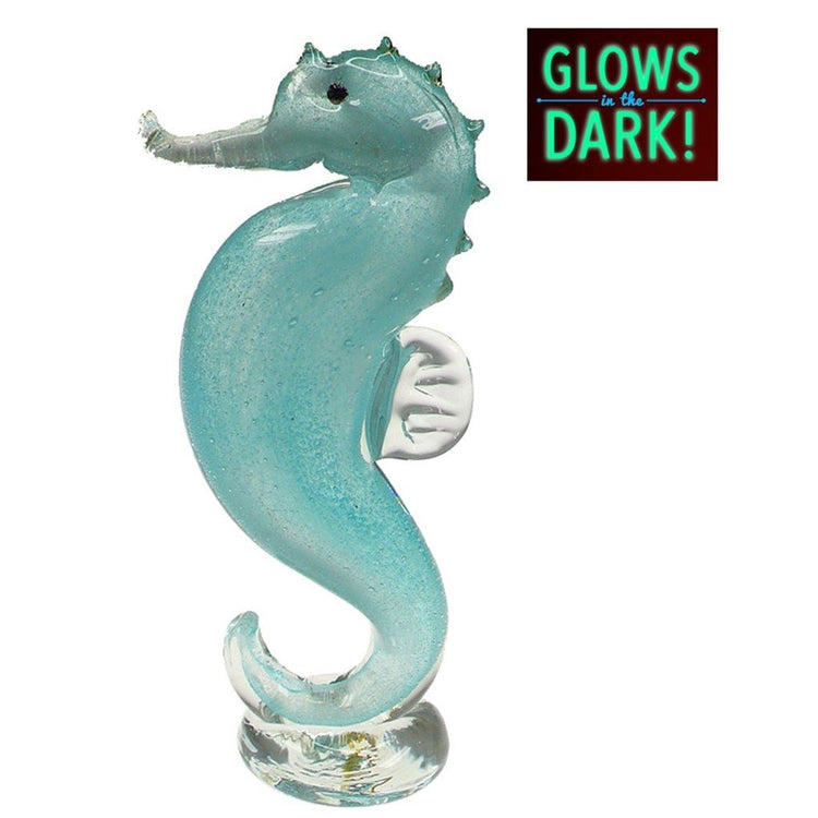Teal glass seahorse standing on tail. seahorse is sitting on clear base. Text in upper corner “Glows in the Dark”