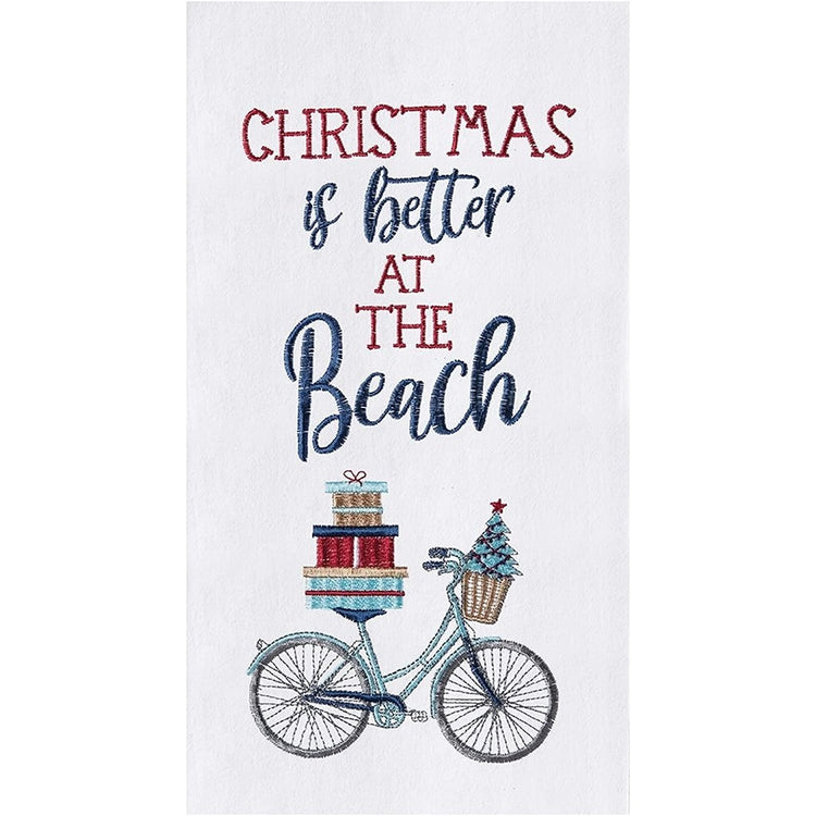 White flour sack towel with embroidered bike with gifts and small tree. the words "christmas is better at the beach" are also embroidered in red and blue.