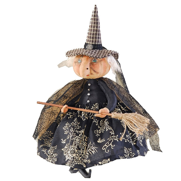 cloth witch holding a broom. Wearing black plaid pointy hat with black dress containing floral pattern