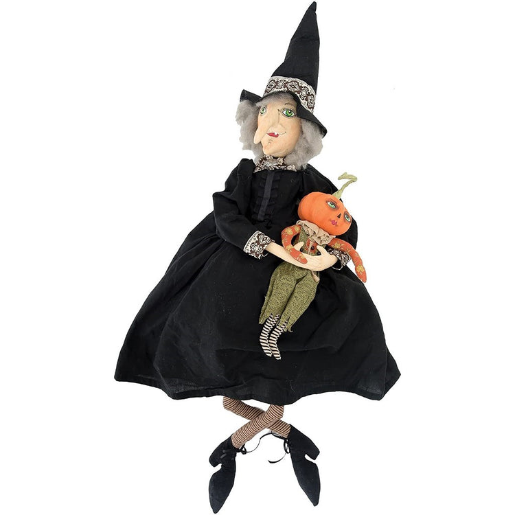 Witch with a black dress & hat holding a baby pumpkin figurine.