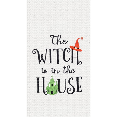 White waffle weave textured hand towel with embroidered words "The witch is in the house" The "H" has an orange witch hat on top & the "O" in house is a green haunted house.
