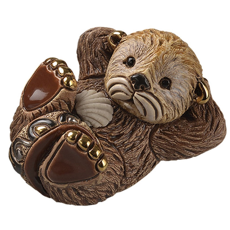 Otter shaped figurine lying on his back with hands behind his head. Browns and gold accent.