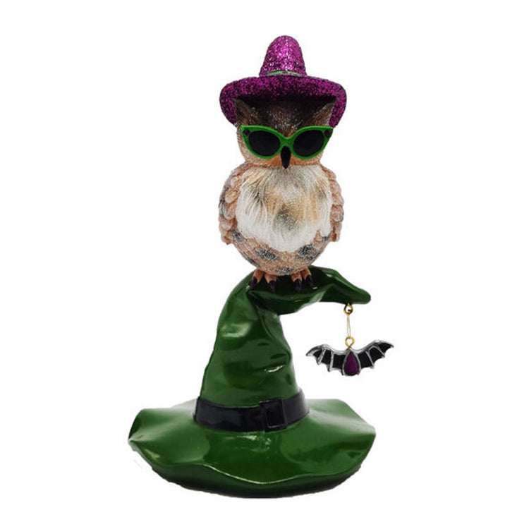 Owl sitting on top of a green witches hat, wearing a purple glittery witch hat and green sunglasses.