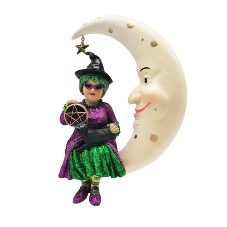 Witch with green hair sitting in a crescent moon. She is wearing a glittery green & purple dress, holding a black cat and a pentagram 