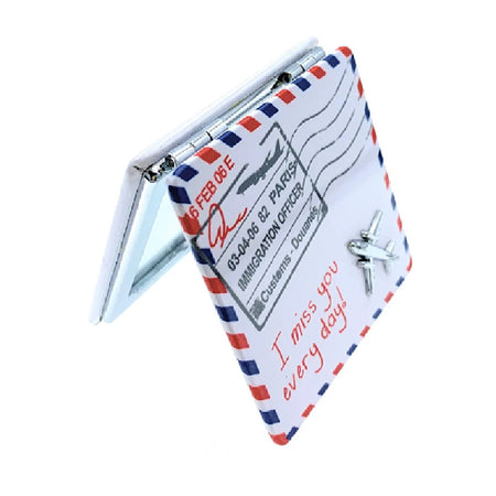 travel size compact mirror, square, designed to look like a piece of mail, white with stamp and small airplane detail.