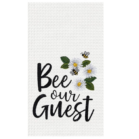 White waffle weave towel with white daisies & bees embroidered on it, black bee our guest words embroidered as well.