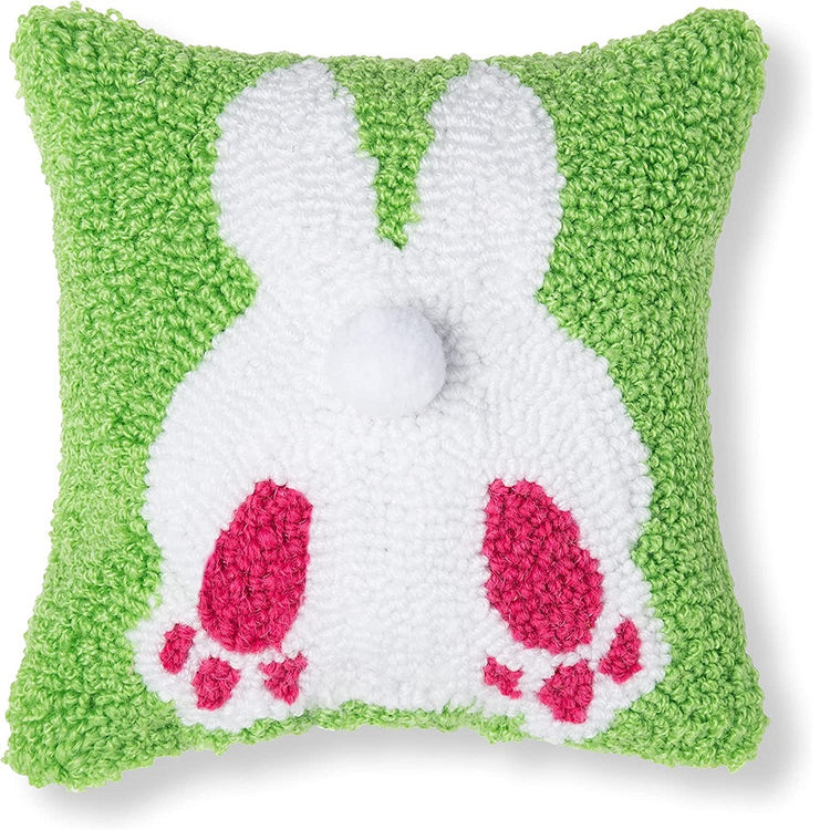 Square pillow with hooked rug type finish. The pillow is green with a view of a white bunny from behind showing a puff tail and pink feet.