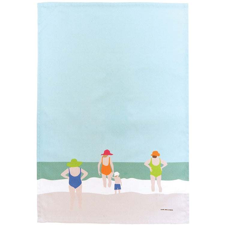 towel with light blue sky, teal water, three ladies and a young boy in bathing suits on the sand.