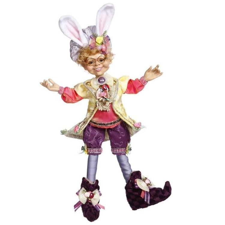 elfin figurine wearing pink top, yellow vest, and purple shorts. His hat has bunny ears on it.