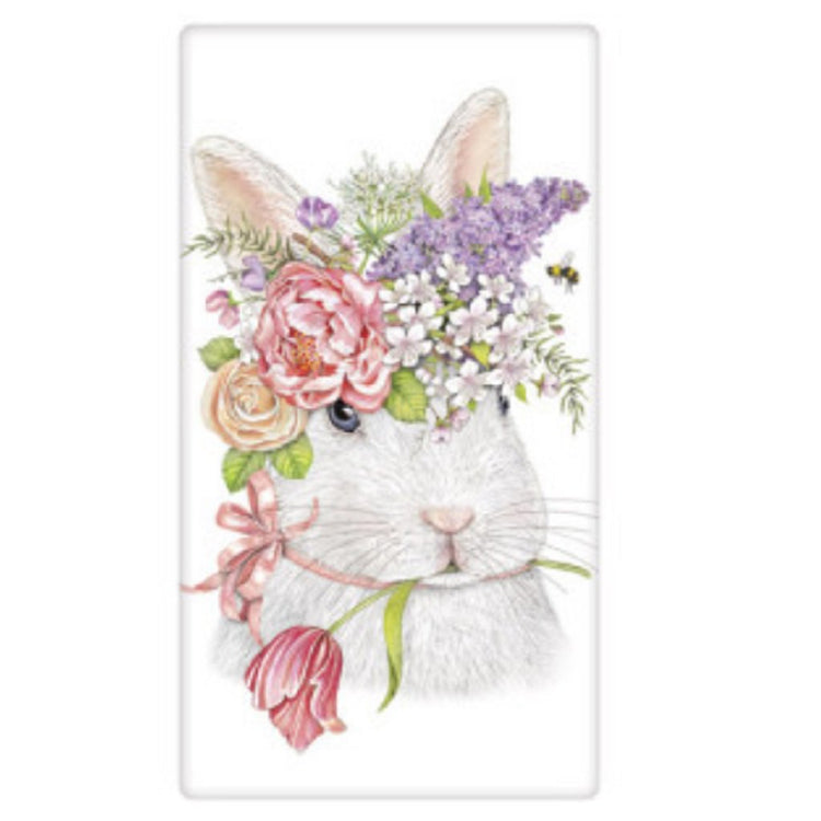 White kitchen towel showing a bunny face. They are wearing a crown of pastel color flowers with a single pink stem in his mouth.  A bumble bee is flying in the flowers.