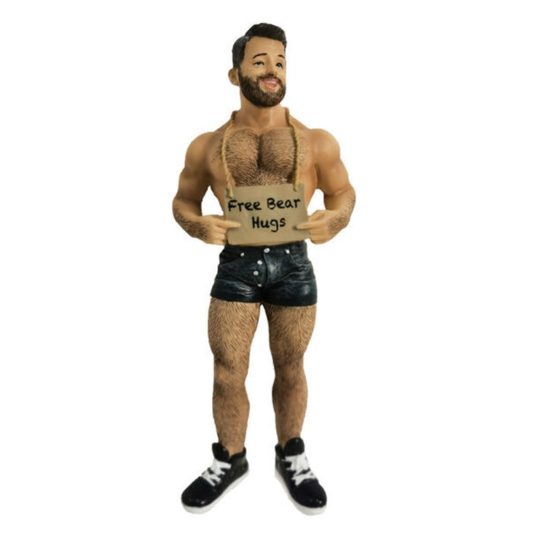 Man with dark brown hair, beard and chest hair, in short black shorts and black shoes, holding sign that says free bear hugs.
