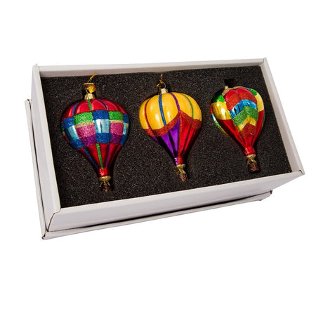 3 blown glass hot air balloon ornaments in a black and gold box. All are rainbow colored with a variety of patterns.