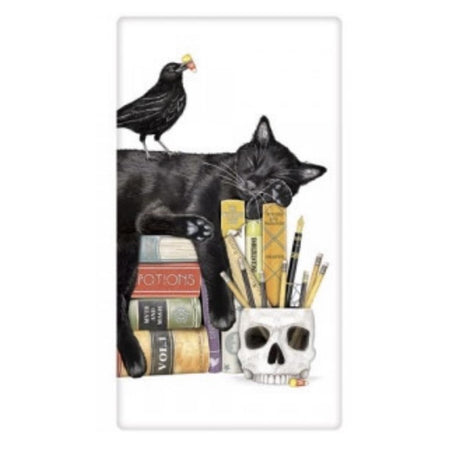 White towel with black cat sleeping on top of a stack of books, and a skull shaped pencil holder.