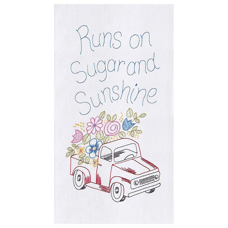 White towel with red truck with blue, yellow, & pink flowers in the bed. Towel says 'Runs on sugar & sunshine'.